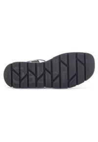 Semelle de chaussure en caoutchouc noir avec un motif de grip texturé. Comprend des crampons surélevés pour la traction et un bord lisse. Logo de la marque visible.