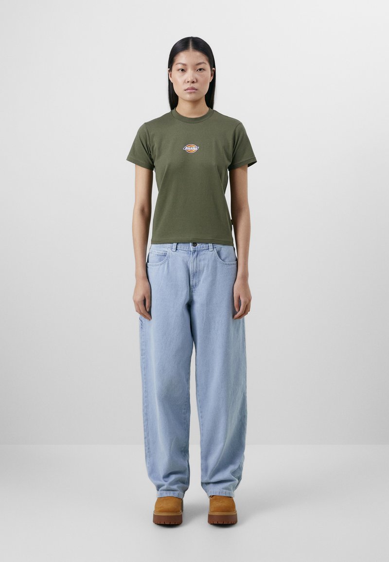 Olive green fitted t-shirt with a round neck and small logo, paired with light blue baggy jeans and tan clogs. Smooth cotton material.