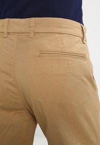 Pantalon kaki en sergé de coton, avec une poche arrière plate à ouverture rectangulaire et des détails cousus à la taille.