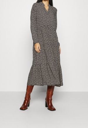 Woman wearing a long-sleeve, black floral midi dress paired with brown heeled leather boots standing against a plain white background.