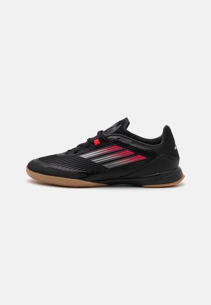 Chaussure de sport noire avec une tige texturée, présentant des accents rouges et argentés, un design profil bas et une semelle en caoutchouc gomme.