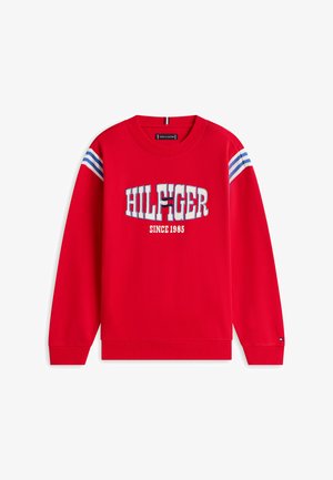 Czerwona bluza z białymi i niebieskimi paskami na ramionach, napis "HILFIGER" oraz logo na piersi, a pod nimi nadruk "SINCE 1985".