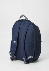 Laikina tamsiai mėlyna kuprinė su dryžuotomis detalėmis ir logotipu. Yra paminkštinti petnešos ir šoninės kišenės. Pagaminta iš tvirto audinio.