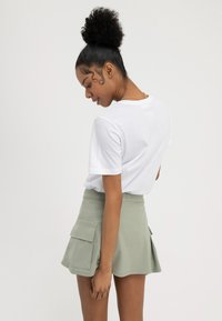 T-shirt blanc à manches courtes associé à une jupe taille haute vert clair avec des poches latérales et un design évasé.