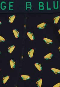 Moške črne bokserice z vzorcem tacos. Imajo zelen elastičen pas z imenom blagovne znamke in barvite ilustracije tacos po vsej površini.