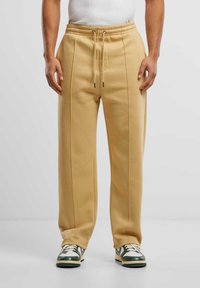 Beige sweatpants met een relaxte pasvorm, voorzien van zijnaad en een elastische tailleband met een trekkoord. Gecombineerd met zwart-witte sneakers.