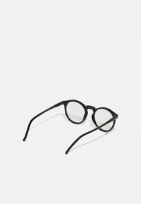 Gafas de sol redondas y negras con un acabado brillante, patas delgadas y lentes transparentes. Un detalle notable es la ligera curva en el puente.