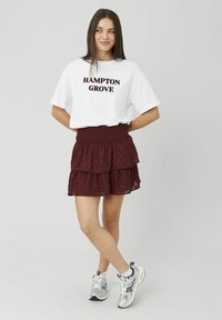 T-shirt blanc avec le texte « HAMPTON GROVE », associé à une jupe à volants bordeaux avec un motif texturé, et des baskets de sport argentées.