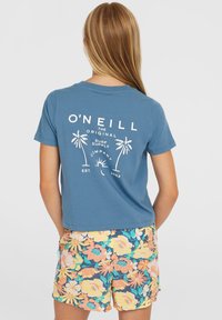 Blaues Baumwoll-T-Shirt mit einem weißen Palmbaum-Graphic und Text auf der Rückseite, kombiniert mit bunten Shorts im Blumendruck.