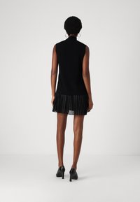 Μαύρο αμάνικο φόρεμα με εφαρμοστό πλεκτό μπούστο και πλισέ διάφανο μαύρο φούστα, συνδυασμένο με μαύρα ψηλοτάκουνα παπούτσια.