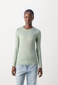Langermet, lysegrønn topp laget av mykt, glatt stoff med rund hals og tettsittende silhuett, sammen med lyseblå jeans.