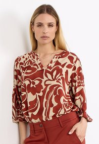 Floral-patterned blouse in beige and rust, featuring a V-neckline, long sleeves, and a relaxed fit with soft fabric texture.