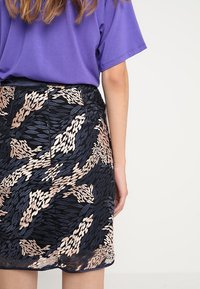 Námořnická sukně s propracovaným zlatým a růžovým vzorem listů, se strukturovanou tkaninou a přiléhavým střihem. Spodní lem je úhledně dokončen.