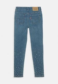 Blå denimjeans med slim fit, subtilt tvättad textur och dekorativa silvernitar längs nederkanten och fickorna.