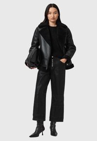 Giacca di pelle nera con colletto in peluche, abbinata a un maglione nero a trama e pantaloni in denim neri a vita alta. Stivali neri con tacco e borsa.