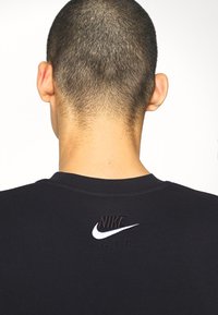 Svart sweatshirt med rund halsringning, som har en strukturerad Nike-logga och "AIR" i svart broderi på övre delen av ryggen.