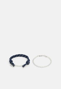 Deux bracelets : un bracelet en corde tressée bleu marine avec des accents verts et un bracelet en chaîne argentée avec une fermeture à clip. Les deux présentent des designs simples.