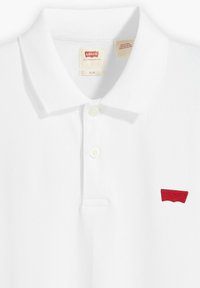 Valkoinen polo-paita, jossa on slim fit -leikkaus, klassinen kaulus, kolme nappia ja punainen brodeerattu logo rinnassa. Kankaassa on teksturoitu pinta.