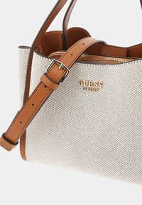 White mesh handbag with tan faux leather straps, featuring a zip closure and gold embossed logo. Compact shape, detailed stitching.