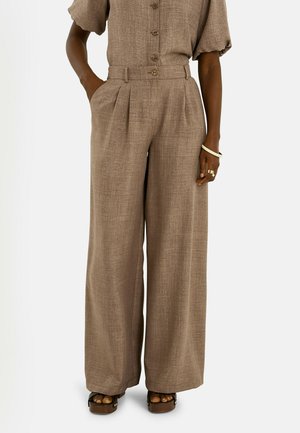 Pantalones marrones de talle alto y pernera ancha con pliegues delanteros, combinados con un top a juego de manga corta con botones y sandalias de plataforma.