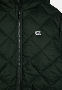 Chaqueta acolchada verde oscuro con cremallera frontal visible y el logotipo bordado en blanco "Lee" en el lado izquierdo del pecho.