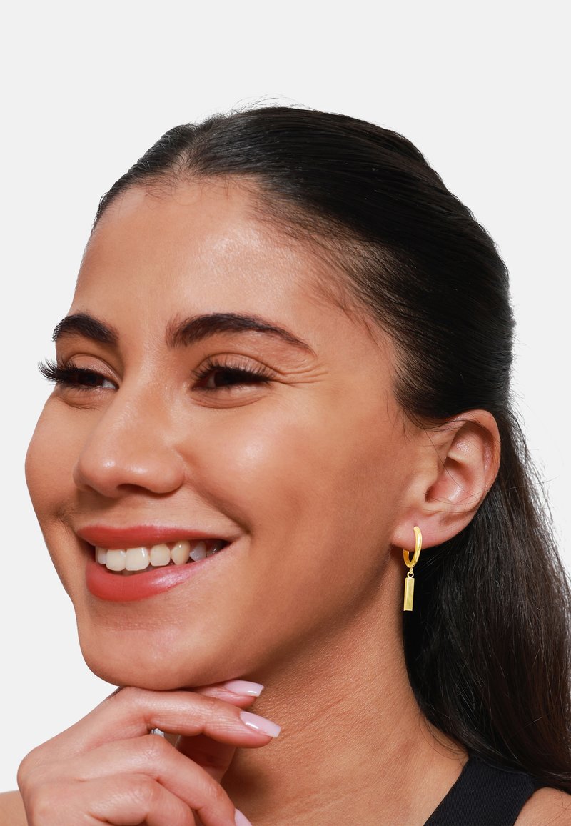Goldene Creolen mit einem vertikalen rechteckigen Anhänger, glatte Oberfläche, glänzende Optik und einem schlichten Design, das das Gesamtbild unterstreicht.