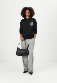 Black sweatshirt with purple floral embroidery on the left chest, paired with gray plaid wide-leg trousers and a black leather shoulder bag.