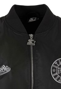 Jachetă bomber neagră cu guler ribbed, închidere cu fermoar argintiu și detalii brodate ale logo-ului. Material neted cu o siluetă subțire.