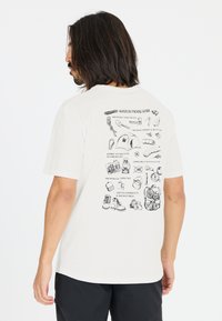 Valkoinen puuvillainen T-paita, jossa on rento leikkaus, takaosassa musta kuvittelu "Whistler Packing Guide" eri vaellustarvikkeista.