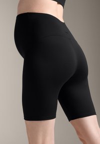 Črne kolesarske hlače z visokim pasom, narejene iz gladkega, elastičnega materiala. Imajo dolžino do sredine stegna in minimalne šive za poenostavljen videz.