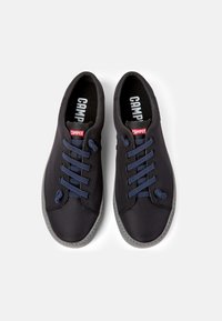 Black fabric shoes with navy laces and a grey rubber sole. Features a red logo tag. Smooth texture with a rounded toe design.
