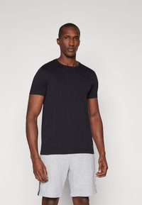 Μαύρη βαμβακερή μπλούζα με στρογγυλή λαιμόκοψη, κοντά μανίκια και κανονική εφαρμογή, συνδυασμένη με γκρι αθλητικά σορτς που έχουν πλαϊνές ρίγες.