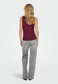 Bordeaux ærmeløs top med en tætsiddende pasform, parret med lysegrå brede jeans med baglommer og en falmet tekstur.
