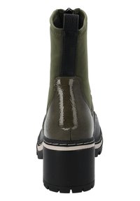 Botín verde con acentos brillantes, parte superior texturizada, tacón grueso y panel trasero negro en contraste. Costura en zigzag a lo largo de la suela.