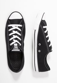 Black canvas sneakers with white laces, rubber toe caps, and side eyelets. Features white stitching and a textured black insole.