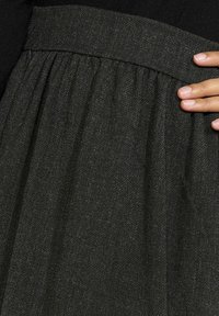 Črna krilka z teksturiranim, tkanim vzorcem, z nabranim materialom na pasu in gladkim pasom. Material ima subtilen sijaj.