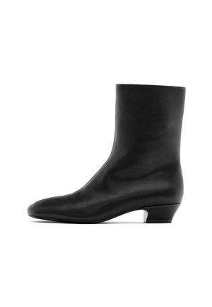 Černá kožená kotníková bota s kulatou špičkou a nízkým asymetrickým podpatkem. Hladký povrch, minimalistický design a žádné viditelné kovové prvky ani akcenty.