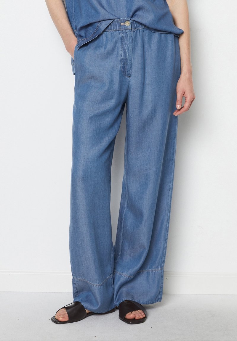 Ljusblå denimbyxor med vida ben, elastisk midja, framfickor och sydd kant. Kombinationen är med svarta sandaler med öppen tå.