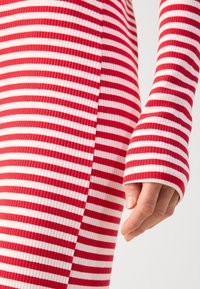 Robe en tissu côtelé rayé rouge et blanc, manches longues, avec une coupe ajustée et un poignet prolongé au niveau du poignet.