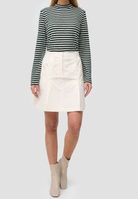 Randig grön och krämfärgad långärmad topp som matchas med en beige kordflodskjol med fickor, åtsittande midja och beiga ankelstövlar.