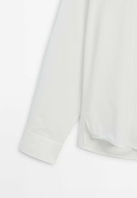 Manche longue blanche de chemise avec poignet et fente latérale visible, présentée sur un fond blanc uni.