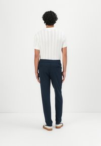 Weißes gestricktes Kurzarmshirt mit vertikalen Streifen, kombiniert mit marineblauen Hosen mit einem Kordelzugbund und zwei Gesäßtaschen.