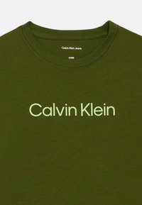 Tricou din bumbac de culoare verde măsliniu, cu guler rotund și mâneci scurte. Prezintă un logo contrastant de culoare verde deschis "Calvin Klein" pe față.