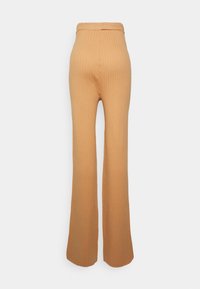 Calças cor de pêssego, com textura riscada, em corte flare, de cintura alta, apresentando um discreto detalhe de costura na parte de trás.