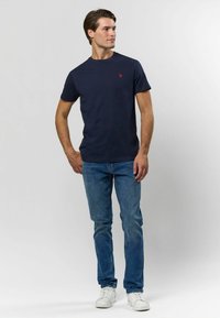 Námořnické tričko s krátkým rukávem, kulatým výstřihem a červeným vyšitým logem. Kombinováno se světle modrými slim-fit džíny a bílými teniskami.