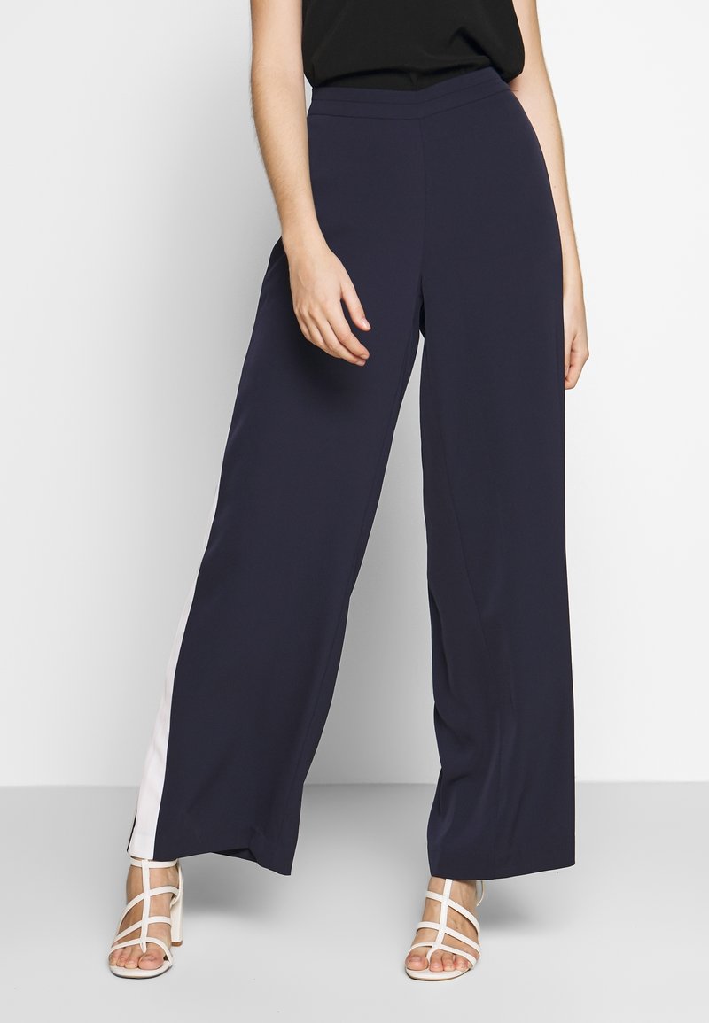 Marinblå vida byxor i mjukt tyg, med en elegant design och vit sidostrand samt en åtsittande midja.