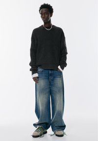 Överdimensionerad ribbad svart tröja med långa ärmar, i kombination med ljusblå baggy denimjeans. Chunky sneakers med gröna detaljer fulländar looken.