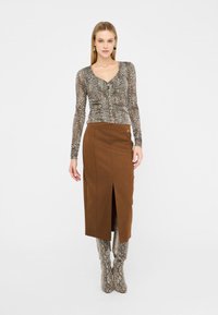 Maglietta a maniche lunghe con stampa leopardata e chiusura a bottoni; gonna marrone al ginocchio con spacco frontale; stivali alti fino al ginocchio con stampa serpente.