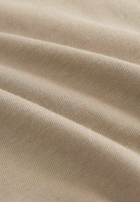 Tela de algodón beige claro con una textura suave, que presenta un sutil ribeteado diagonal y un suave caída.