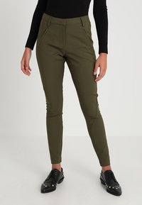 Olivgrön slim-fit byxor i ett smidigt tyg, med framfickor och hög midja, parat med svarta nitar skor.